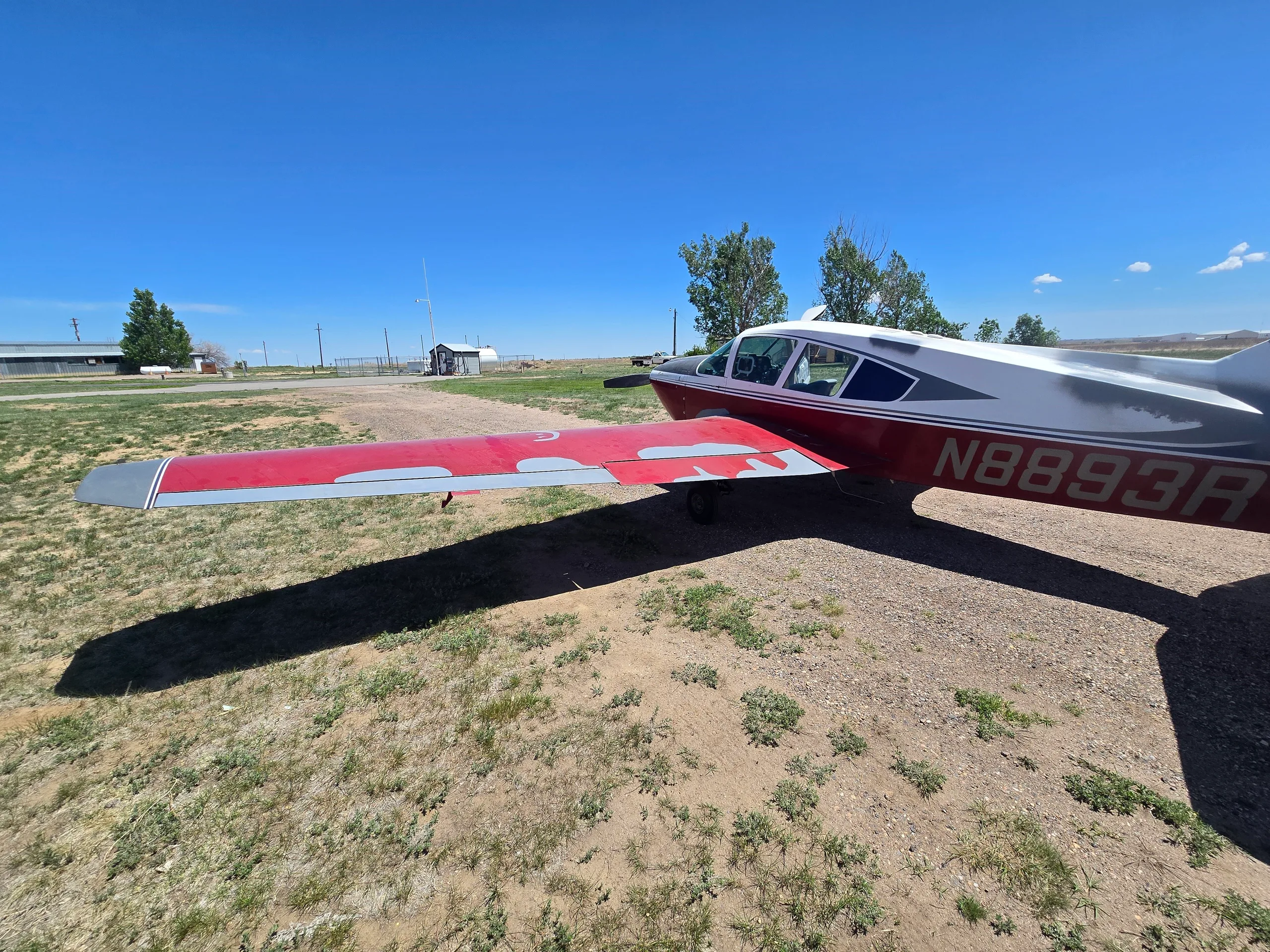 A red and silver single-engine aircraft, registration N8893R, viewed from the rear-right, highlighting the wing and tail.