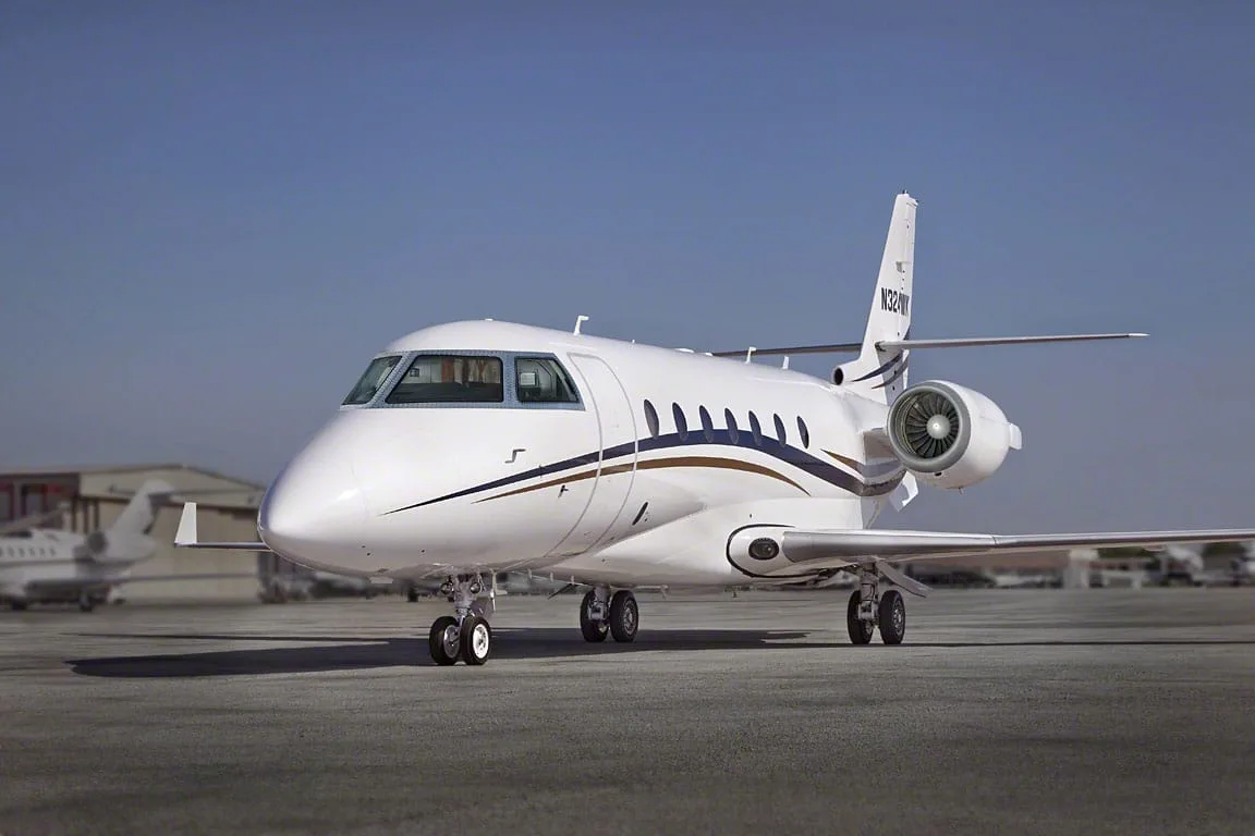 A white business jet with blue and gold stripes and tail number N324WK parked on a tarmac under a clear blue sky.
