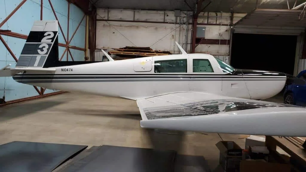Rear-side view of a white and black Grumman American AA-5 Traveler aircraft, N1047A, inside a hangar.