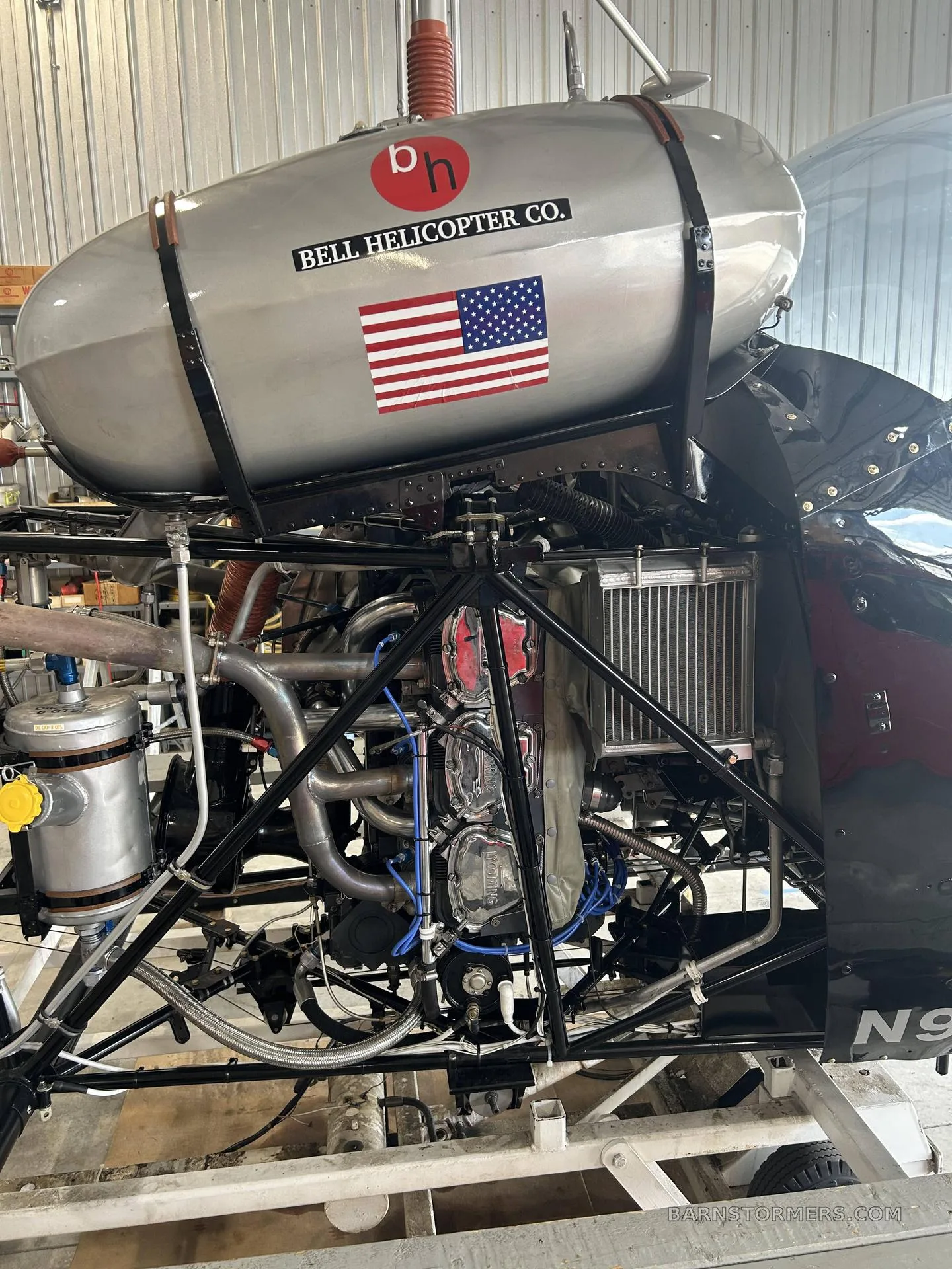 The engine and fuel tank of a Bell helicopter, showing exposed mechanical components and a US flag sticker.