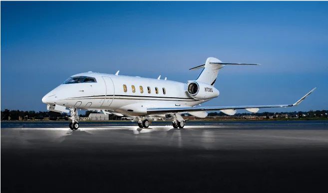 A white Bombardier Challenger 350 business jet with registration N708U is parked on an airfield at dusk.