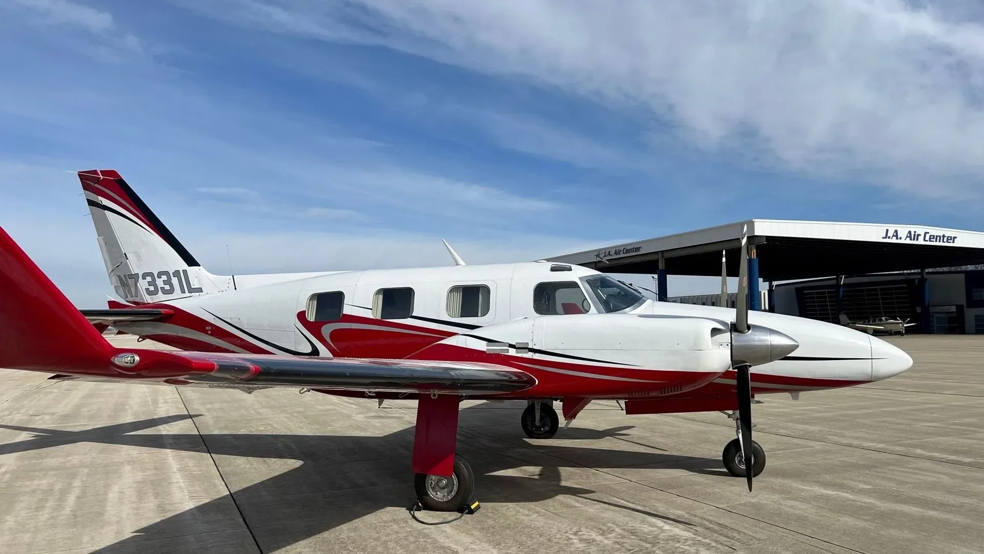 A white and red single-engine propeller aircraft, tail number N7331L, parked on an airfield tarmac with a hangar in the background.