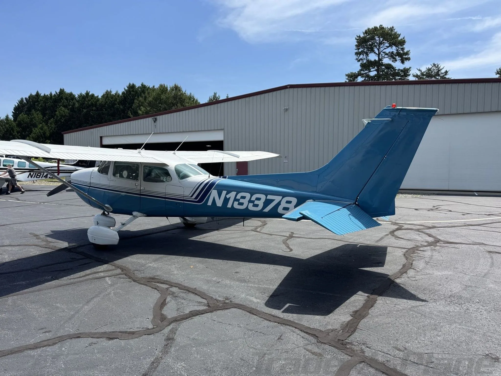A rear-left view of the blue and white Cessna 172 Skyhawk (N13378) parked on an asphalt apron.