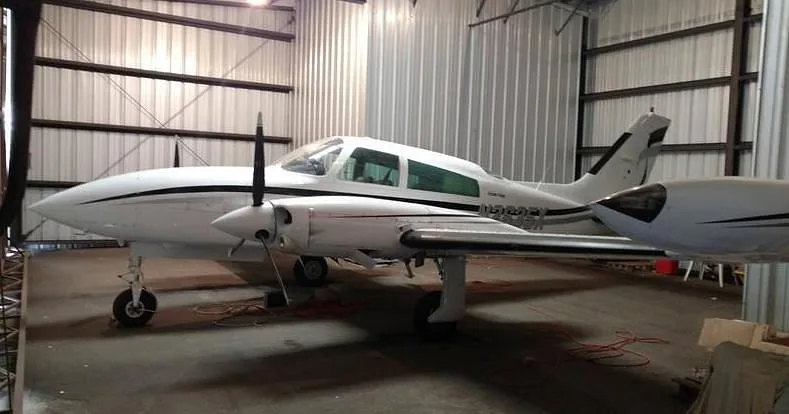 A white twin-engine aircraft, N2635X, with black and gray stripes, parked inside a metal hangar.