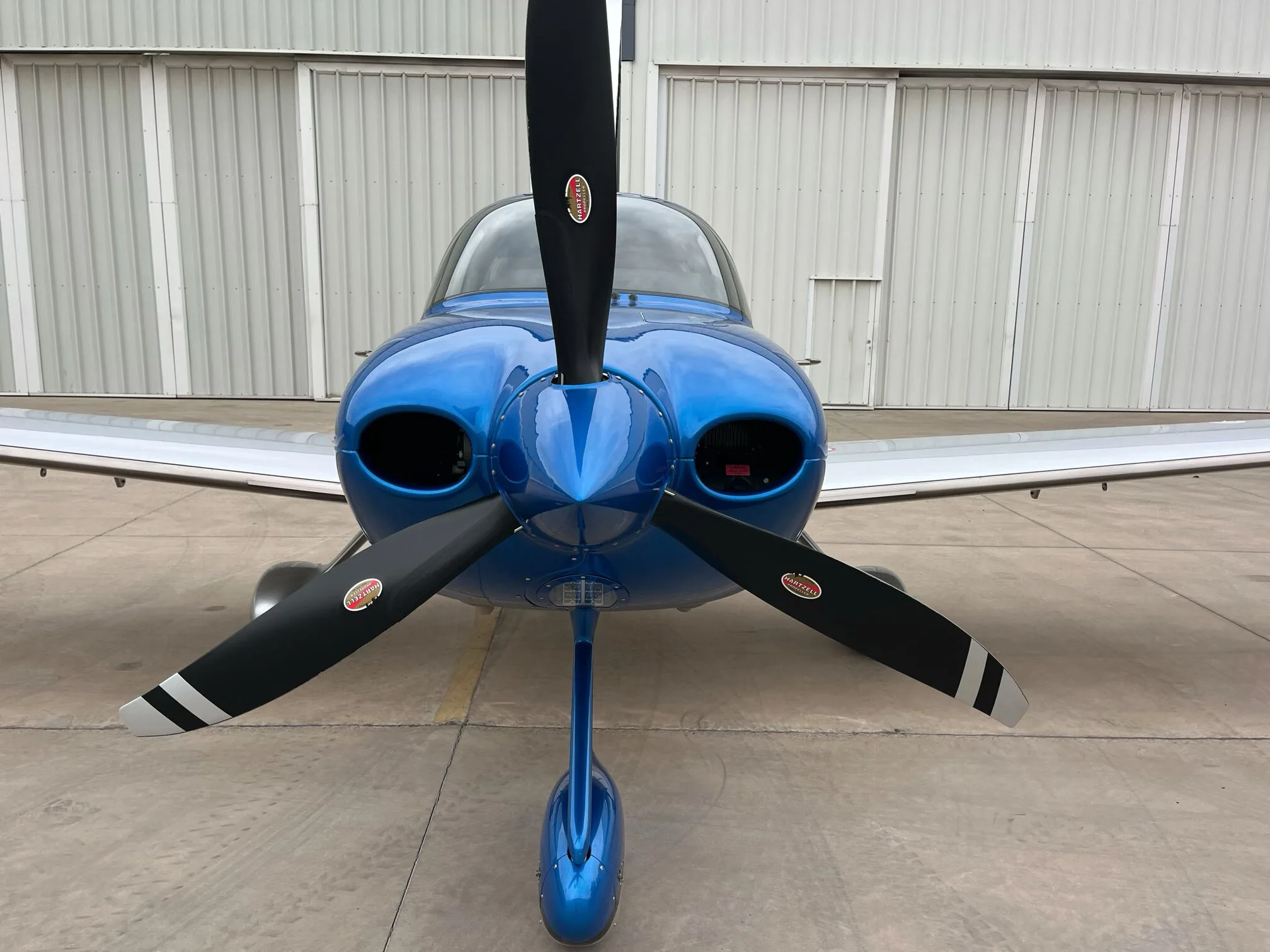 A head-on view of the blue and silver Cirrus SR22 GTS aircraft, highlighting its propeller and nose.