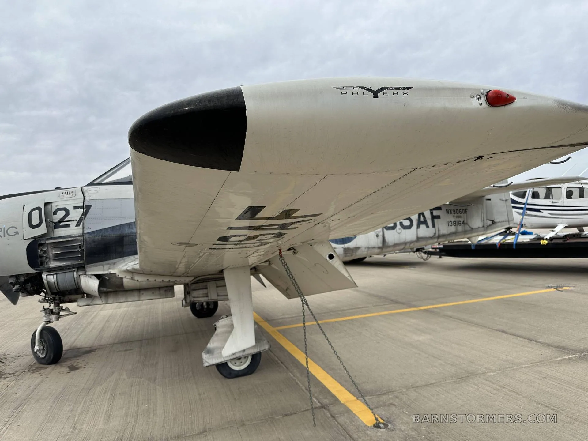 A low-angle view of the wing and landing gear of a gray military trainer aircraft, possibly a T-28 Trojan, parked on an airfield.