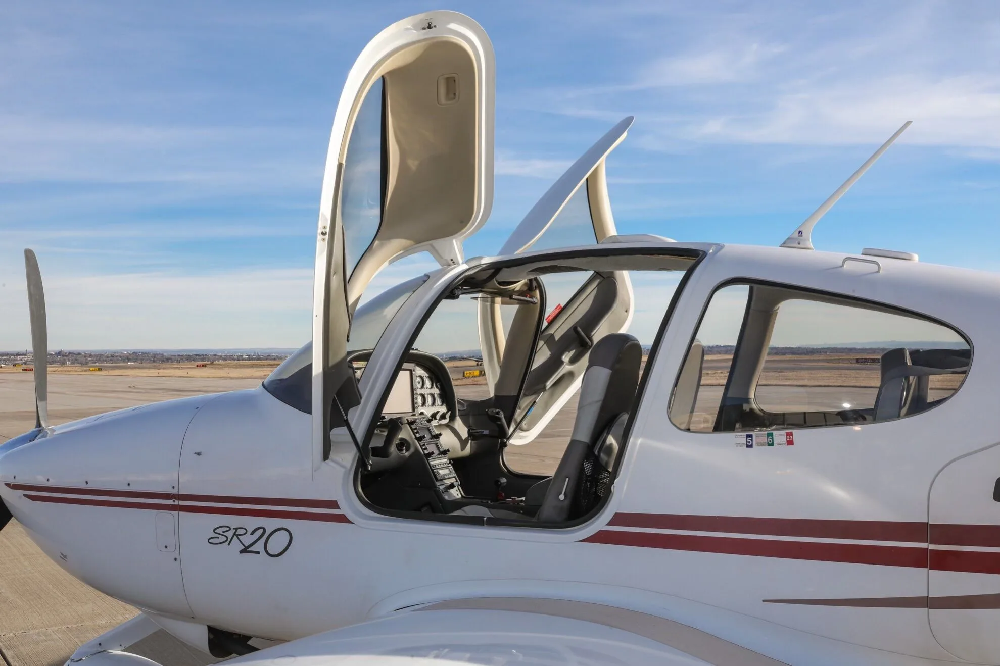Close-up side view of a white Cirrus SR20 aircraft with its gull-wing doors open, showing the cockpit and cabin interior.