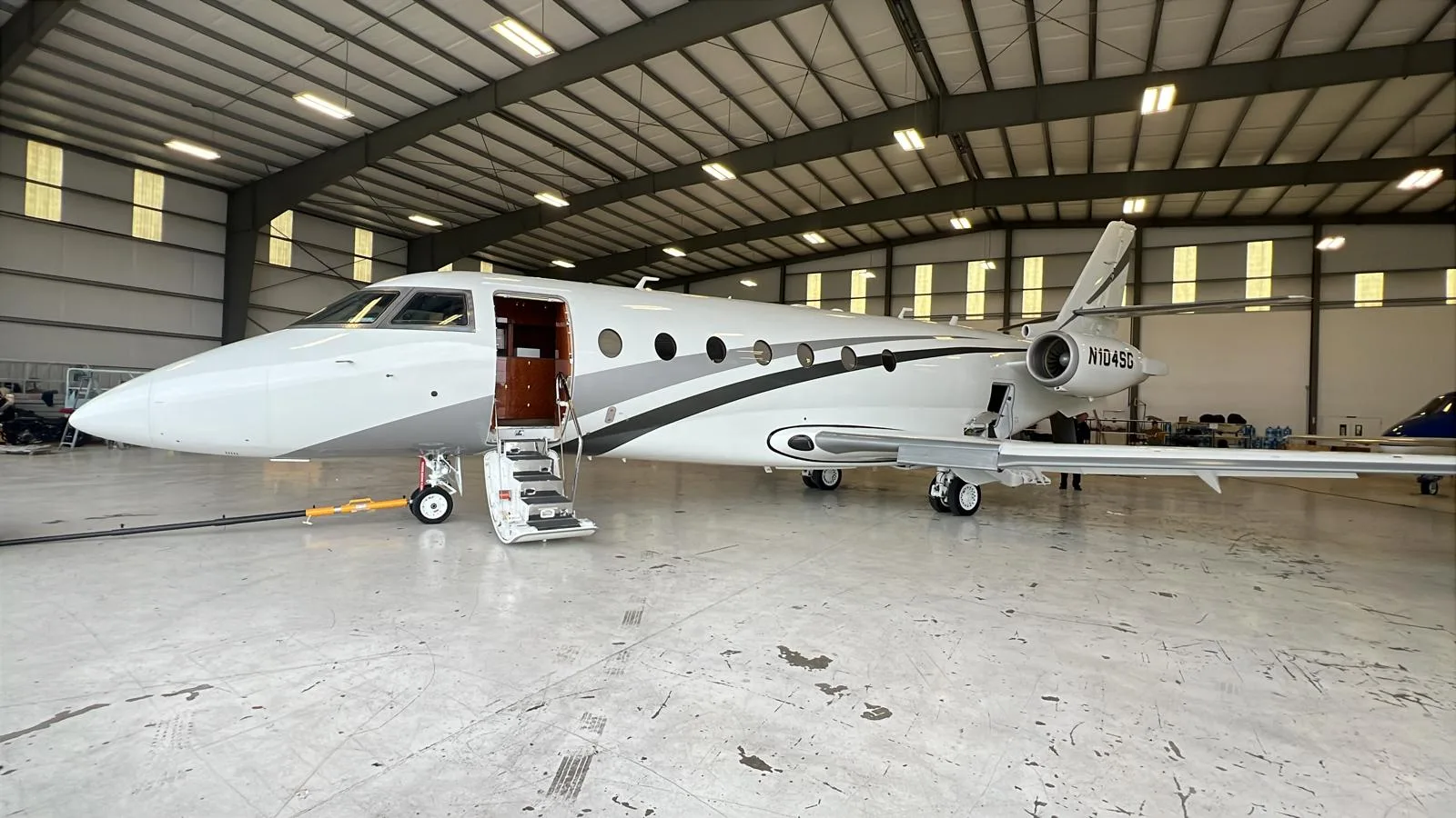 A white and gray jet with tail number N104SG sits inside a hangar with the door open.