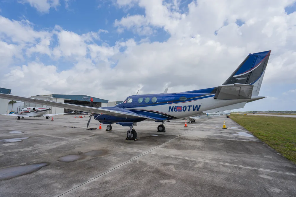 A blue and white twin-engine turboprop aircraft, N620TW, parked on a wet tarmac with hangars in the background.