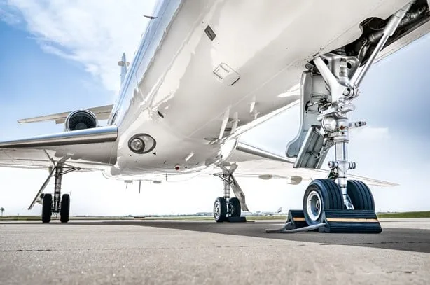 A low-angle view of the main landing gear and underside of a white business jet on an airport tarmac.
