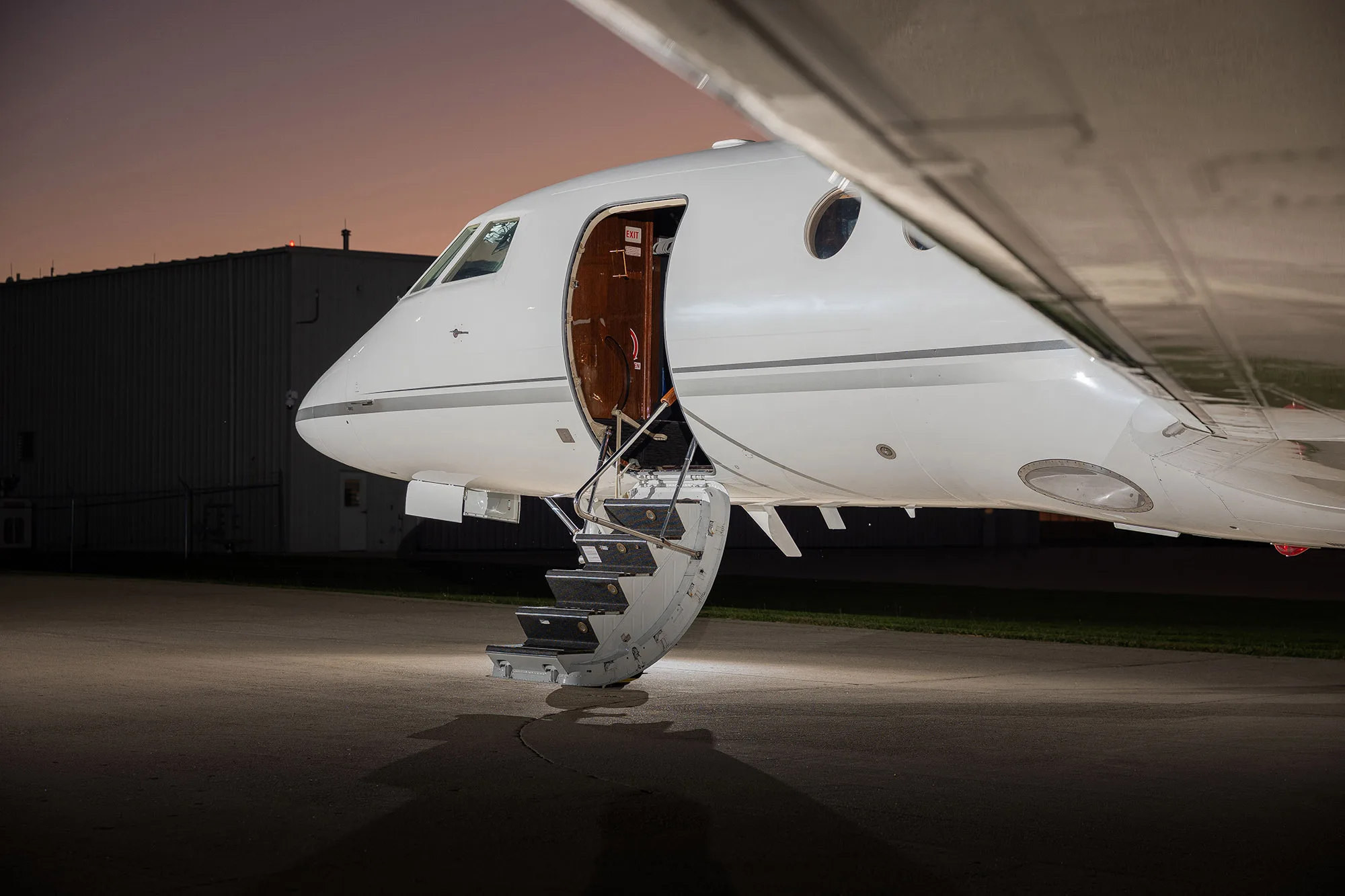 The open main entry door and airstairs of a white Dassault Falcon 900EX business jet (N803NL) at dusk.