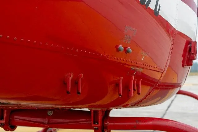 A close-up of the red fuselage section of the helicopter, showing rivets and small external details.
