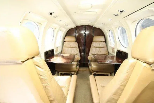 The interior cabin of an aircraft with tan leather seats and small tables.