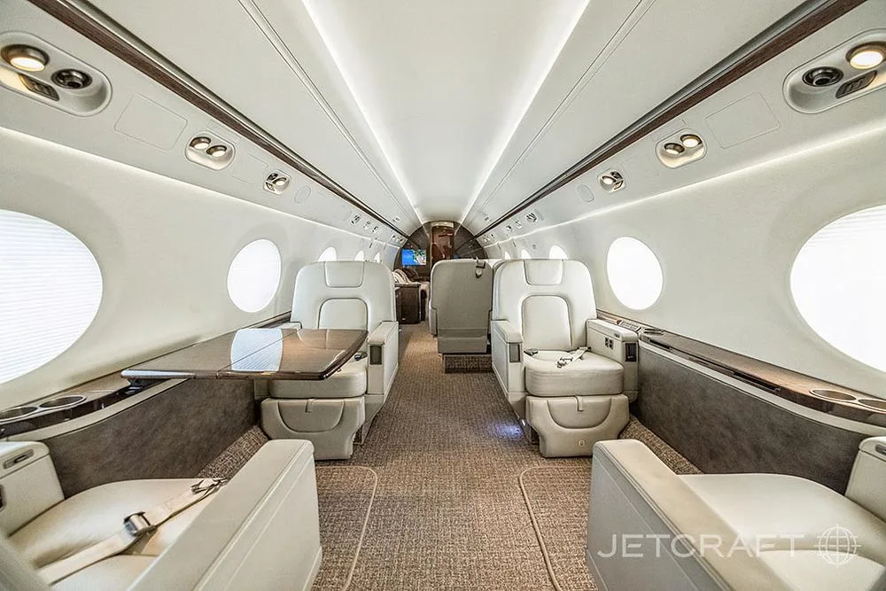 A view of the Gulfstream G650 cabin interior showing cream leather seats and a polished wooden table.
