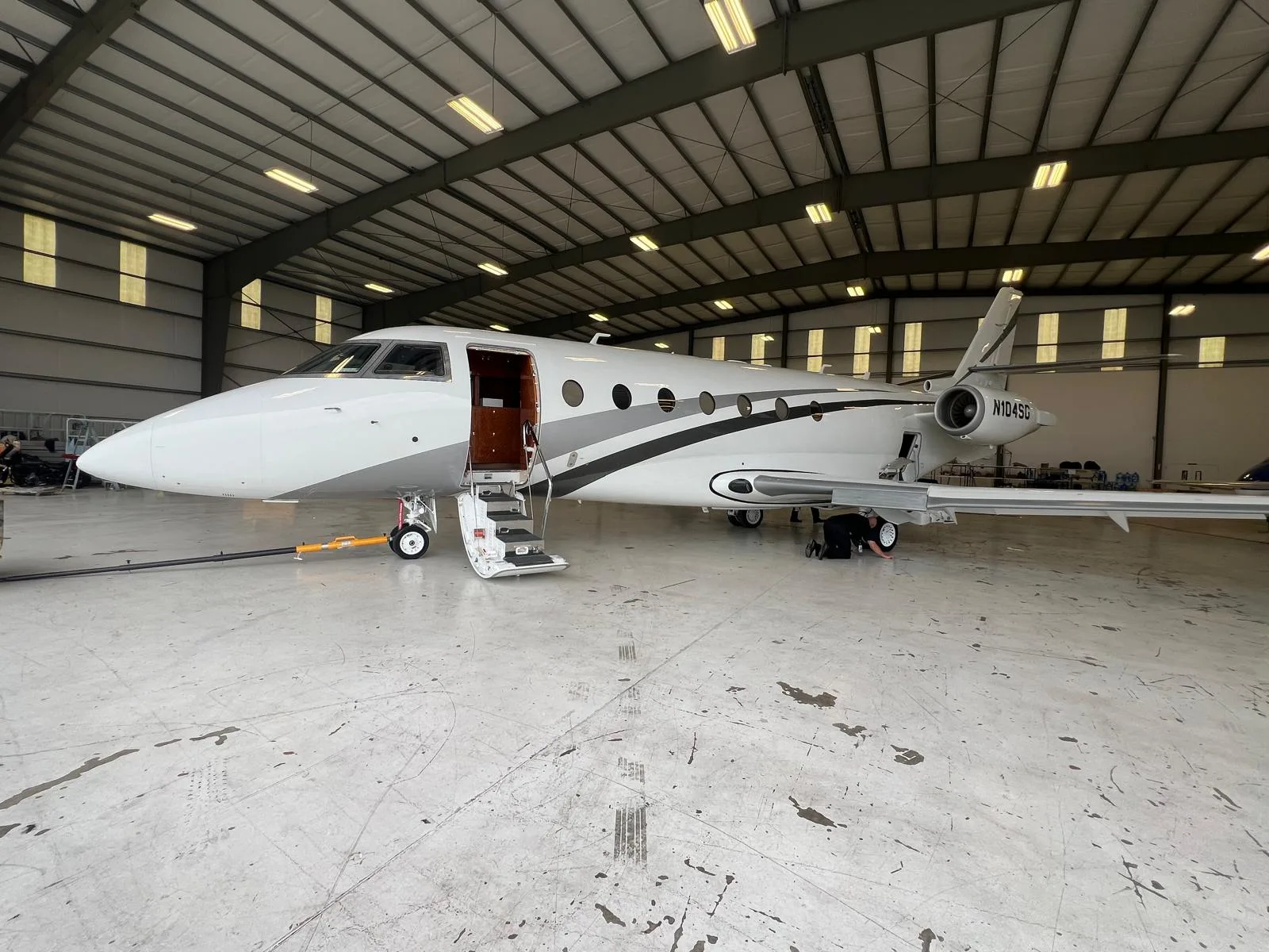 A white and gray jet with tail number N104SG sits inside a hangar with the door open.