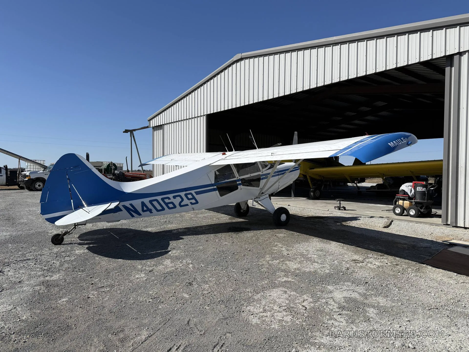 A white and blue Maule aircraft (N40629) parked outside an open hangar, viewed from the rear-left side.