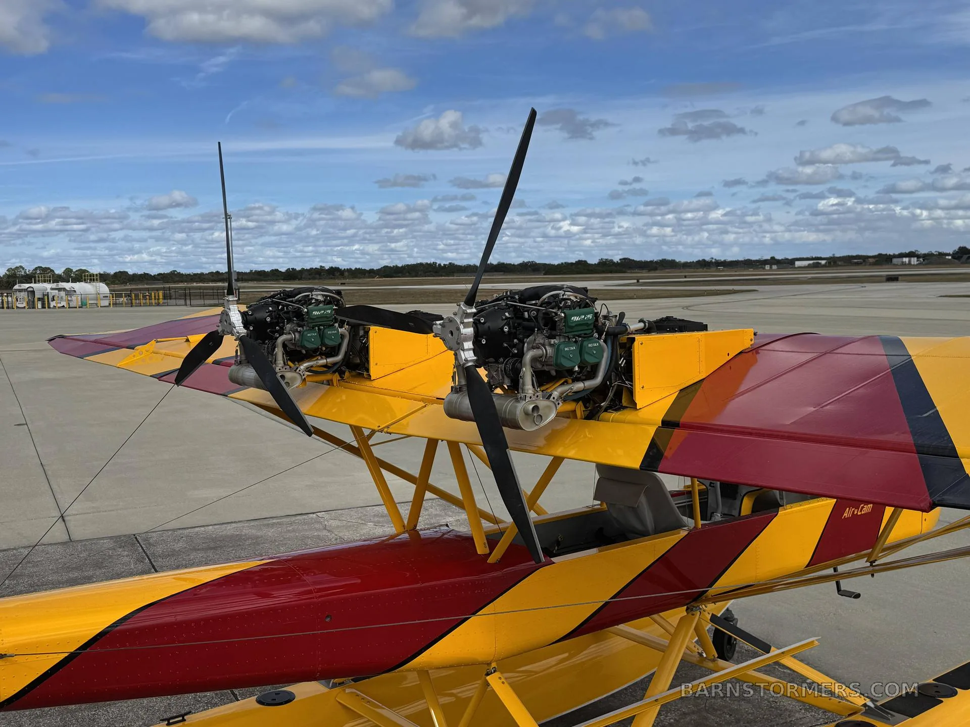 A close-up view of the two exposed engines and propellers mounted on the wing of a yellow and red Air-Cam seaplane.