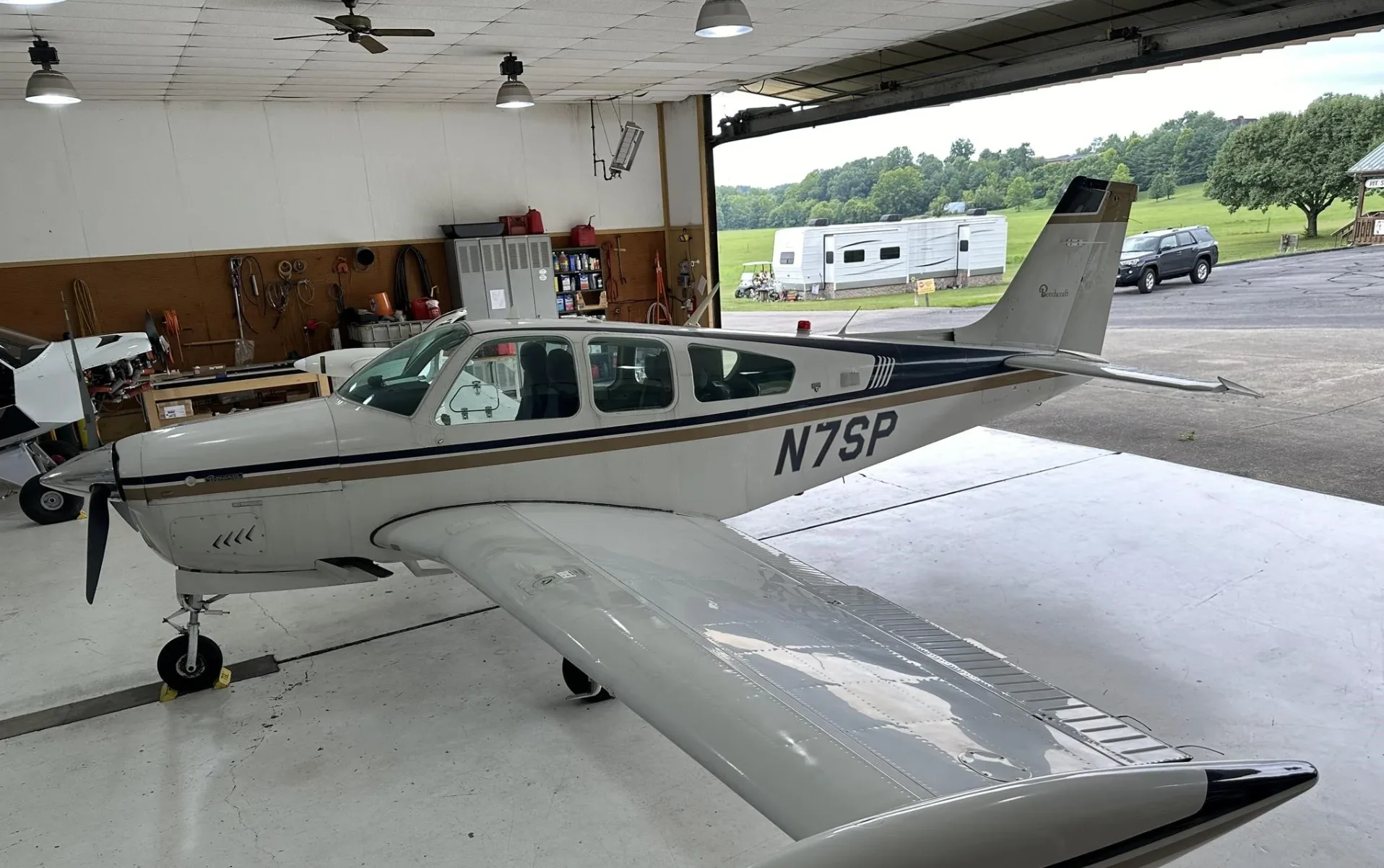 A white and gold Beechcraft Bonanza N7SP parked in a hangar, viewed from the rear right.