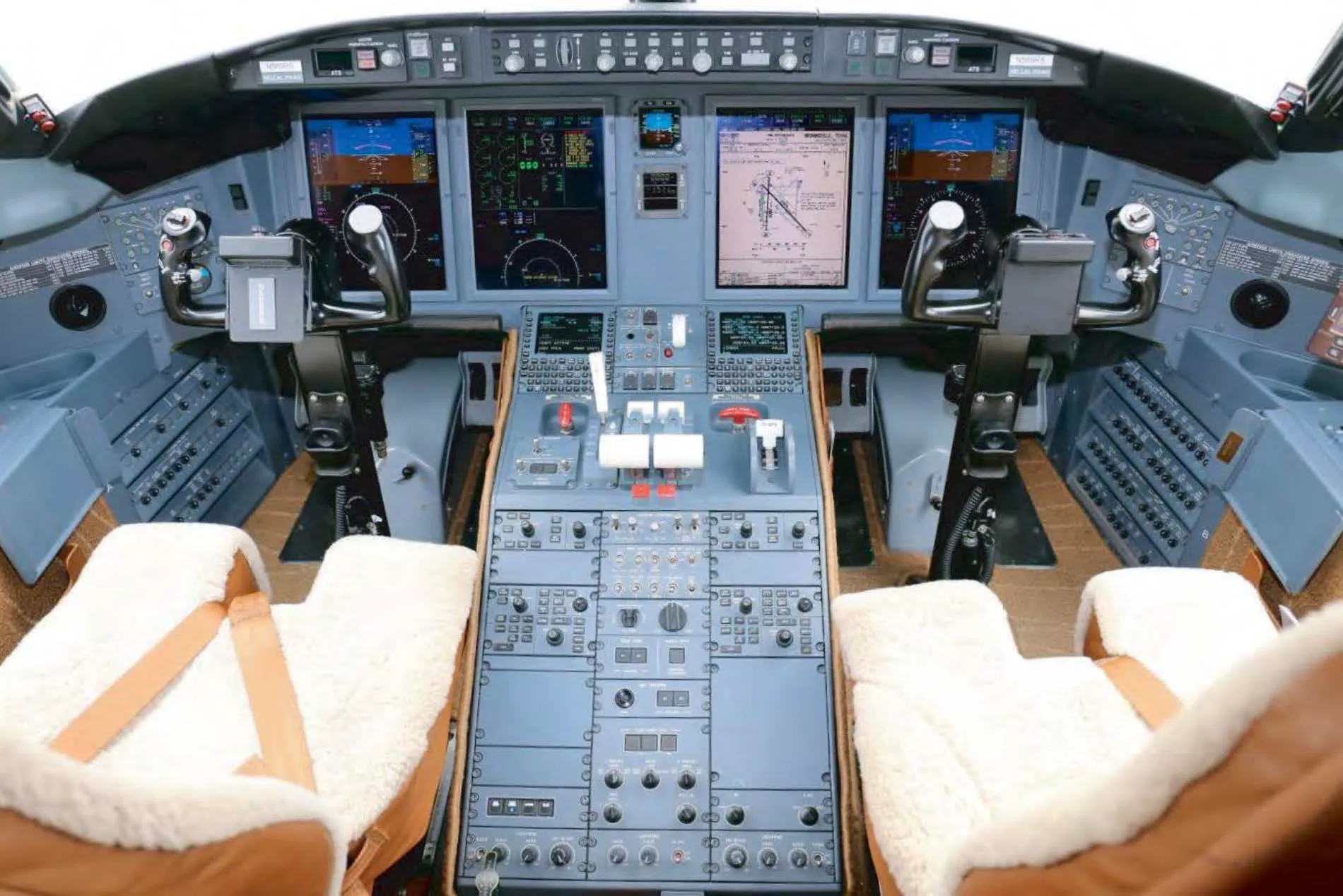 The cockpit of a business jet, showing the instrument panel, controls, and two pilot seats with sheepskin covers.