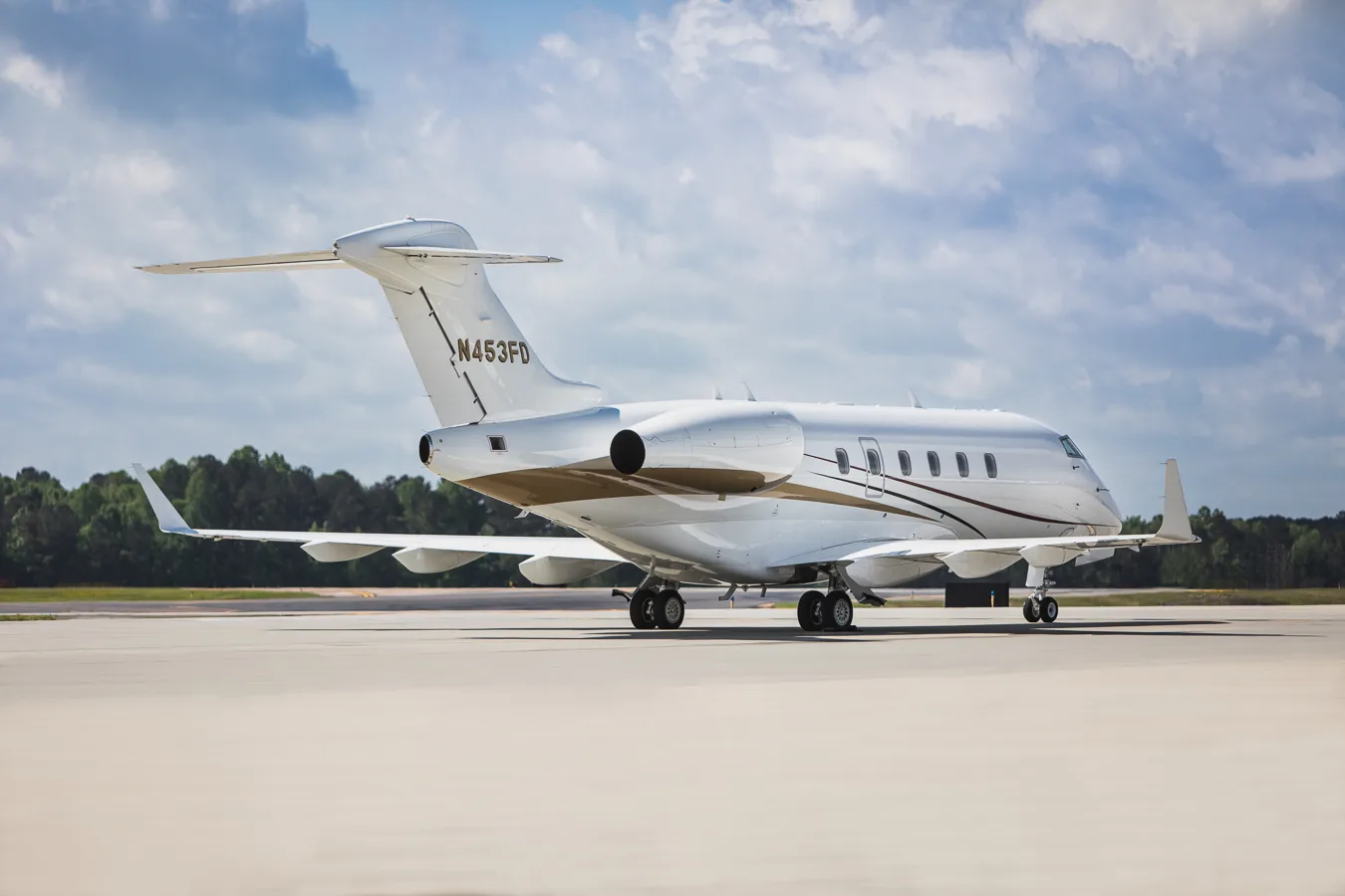 Side view of a white business jet with N453FD registration, featuring gold and maroon stripes, parked on an airfield.