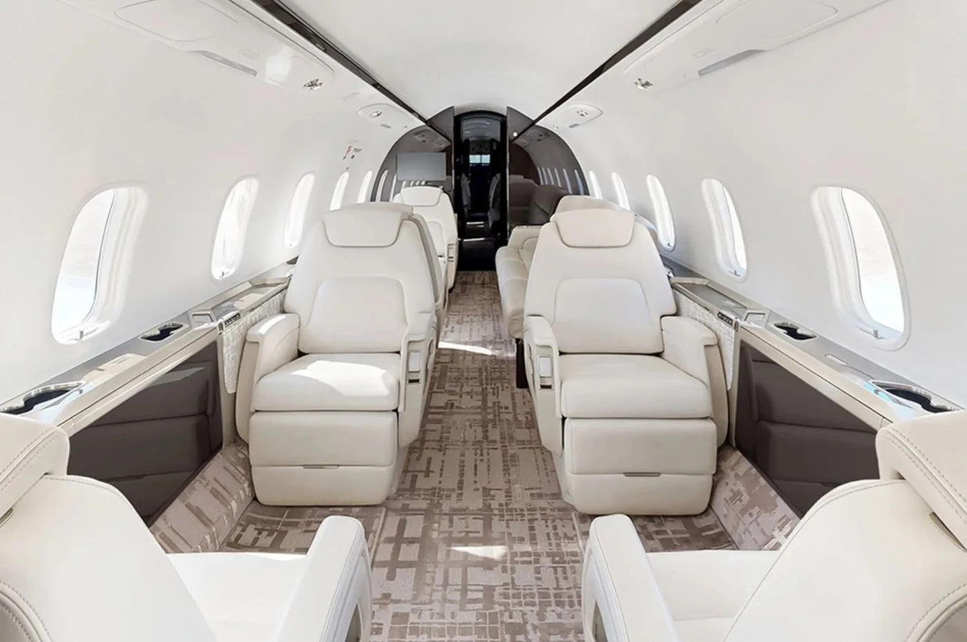 The luxurious interior cabin of a private jet with white leather seats and patterned carpet.