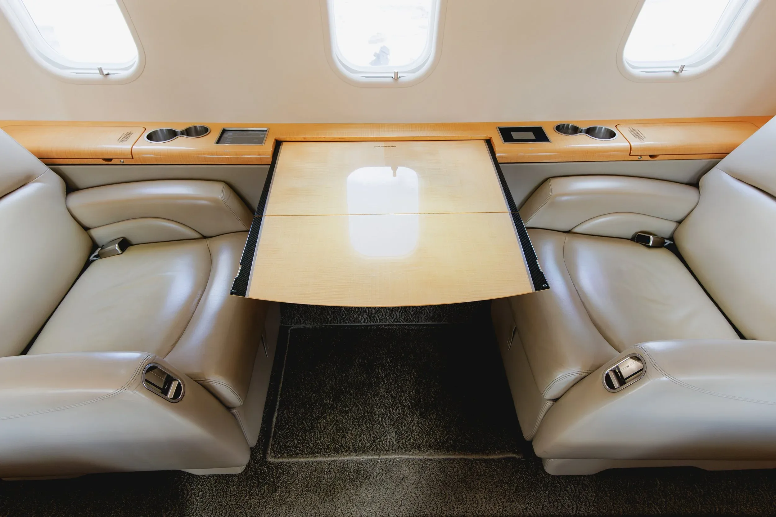 A light wood table extended between two light beige leather seats in a private jet cabin.