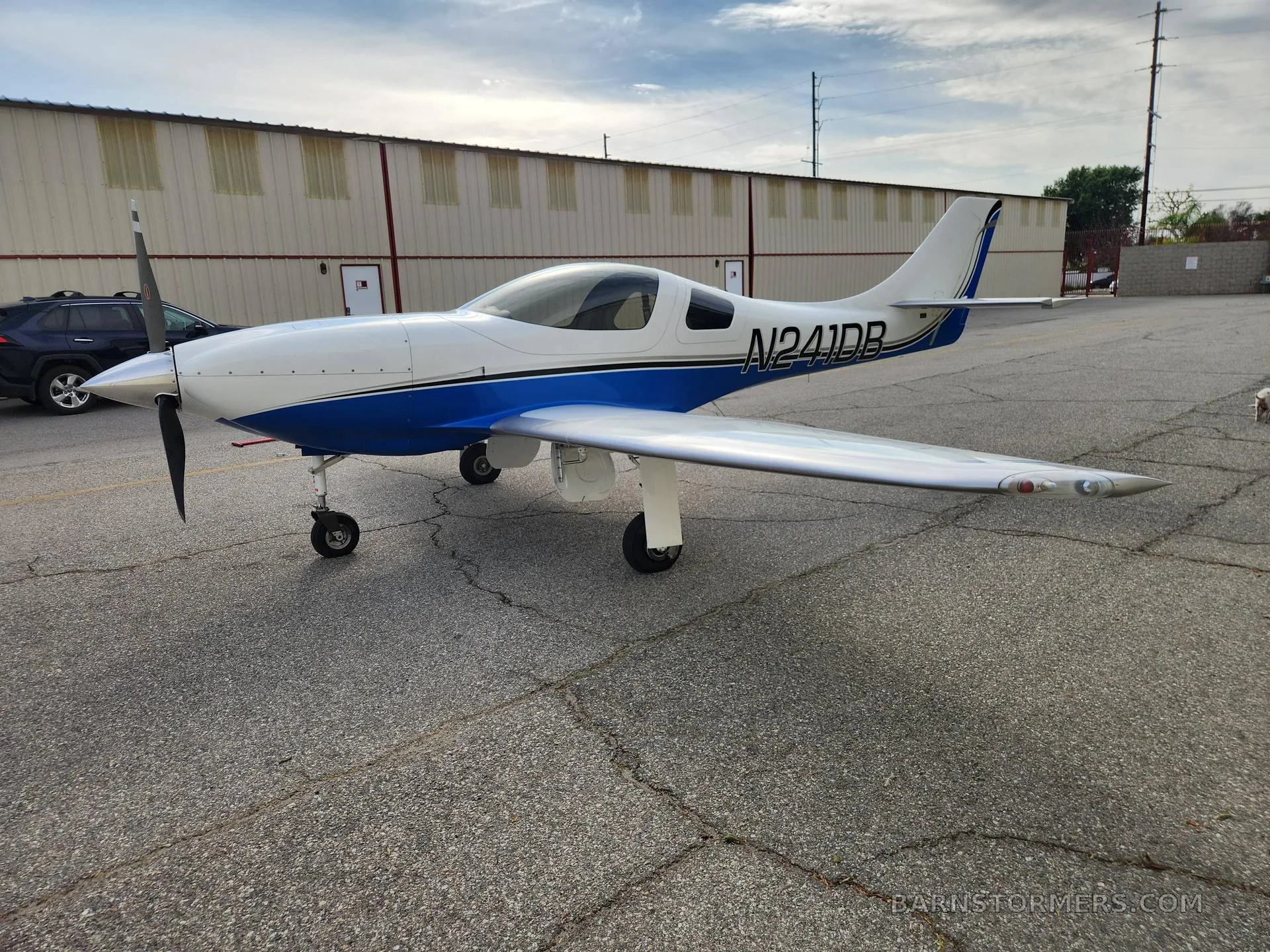 A white and blue single-engine aircraft with registration N241DB, parked on a tarmac with buildings in the background.