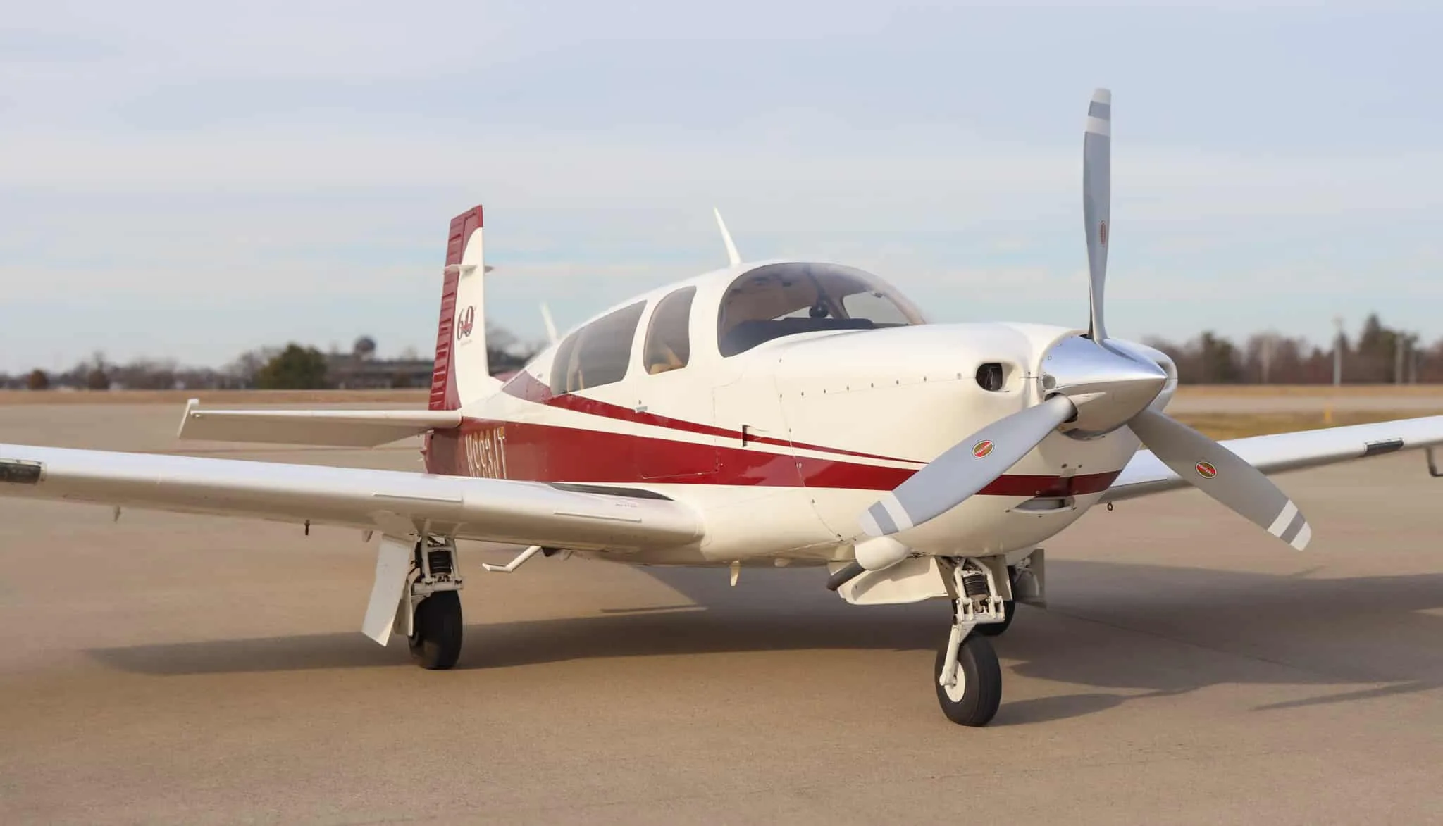 Front three-quarter view of a white and red single-engine propeller aircraft, N993JT, on an airfield.