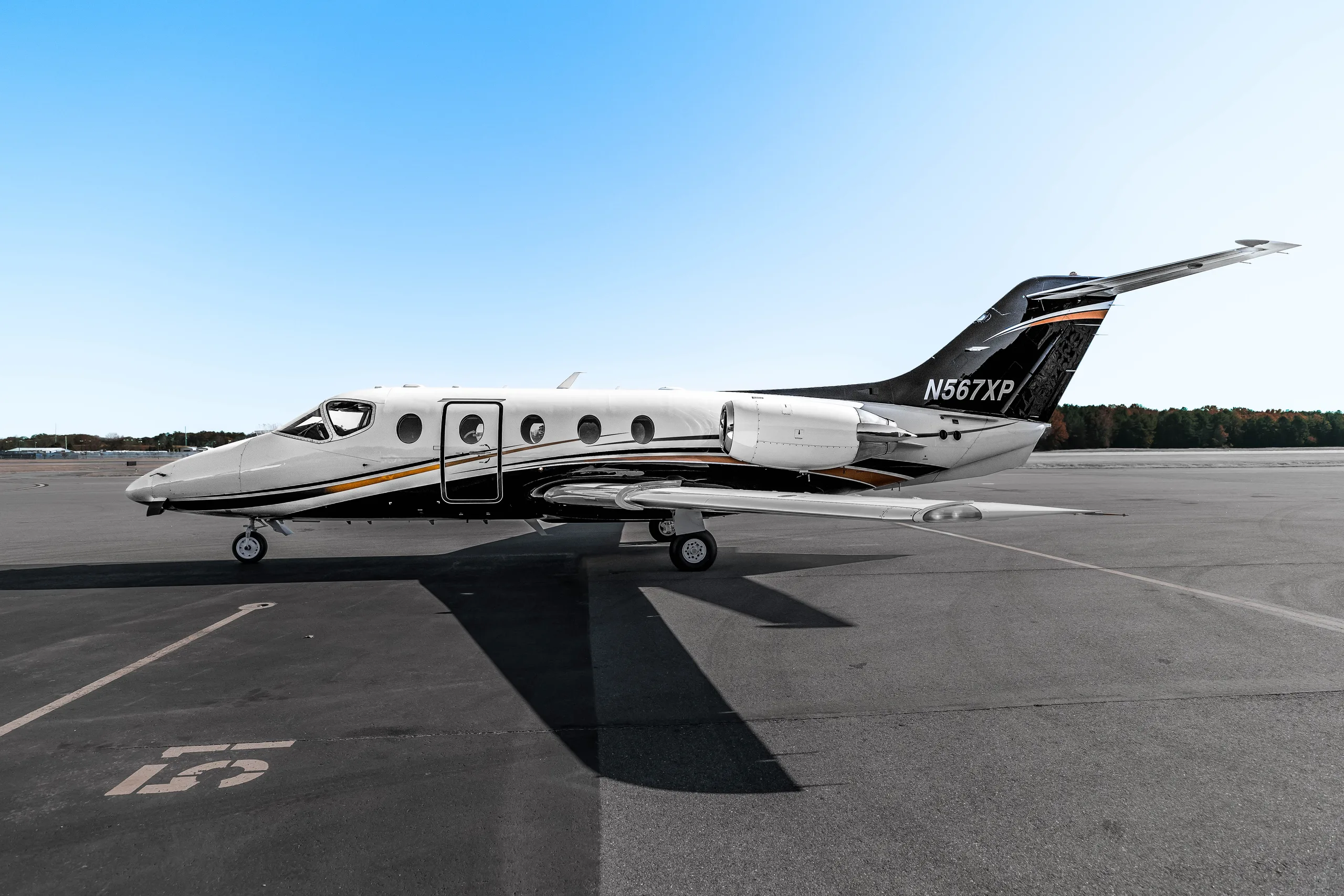 A white and black private jet with gold and white accent stripes is parked on an asphalt tarmac under a clear blue sky.
