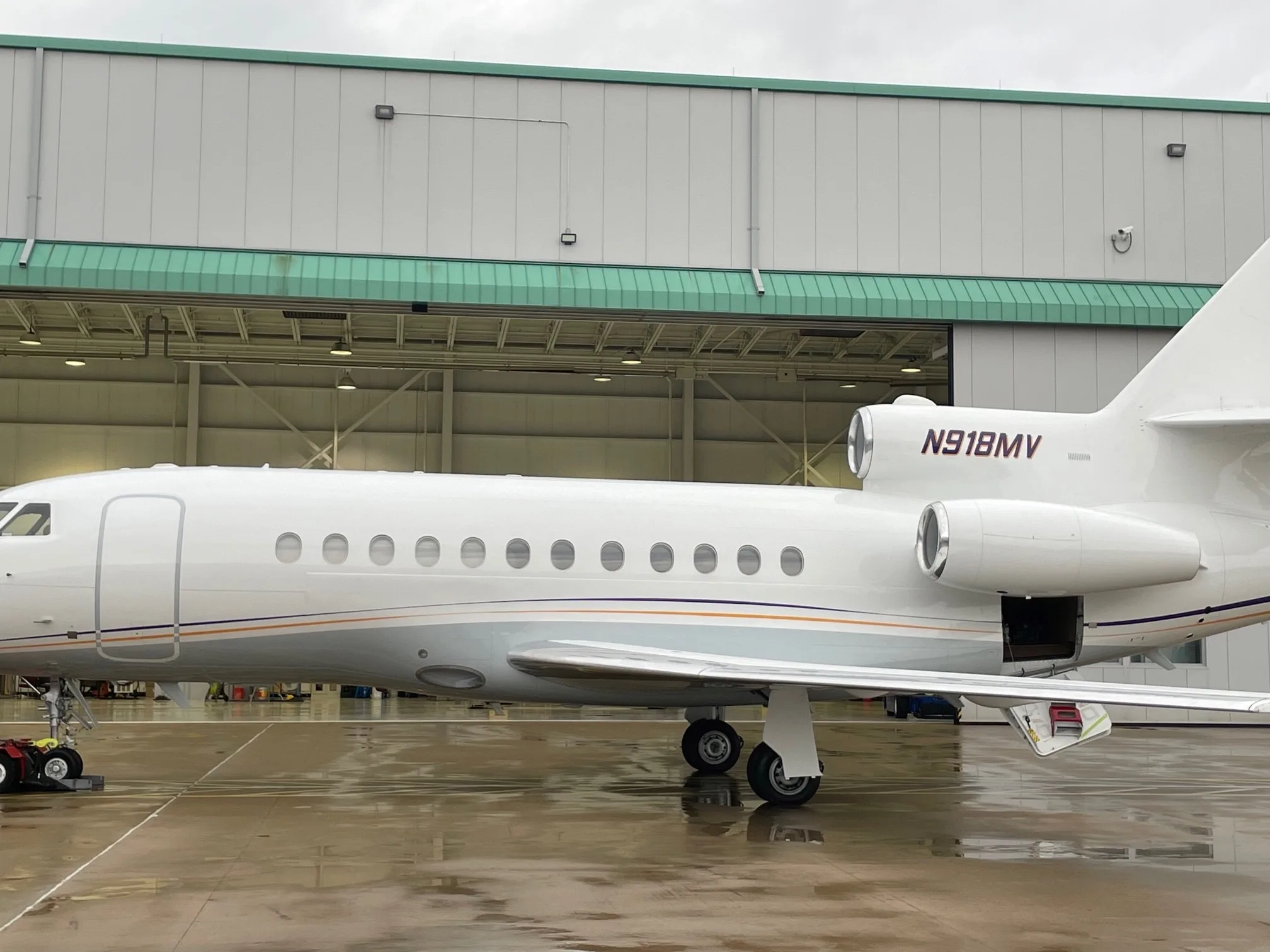 A Falcon aircraft with registration N918MV is parked outside a hangar.