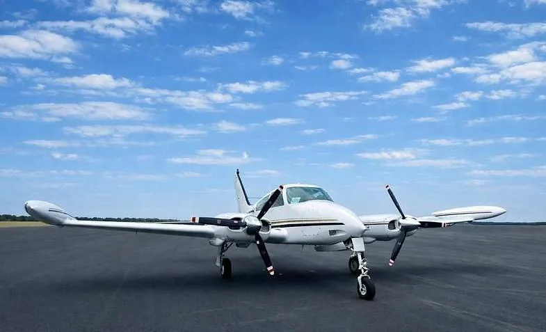 A white twin-engine propeller aircraft with black and gold stripes on an asphalt runway under a blue sky.