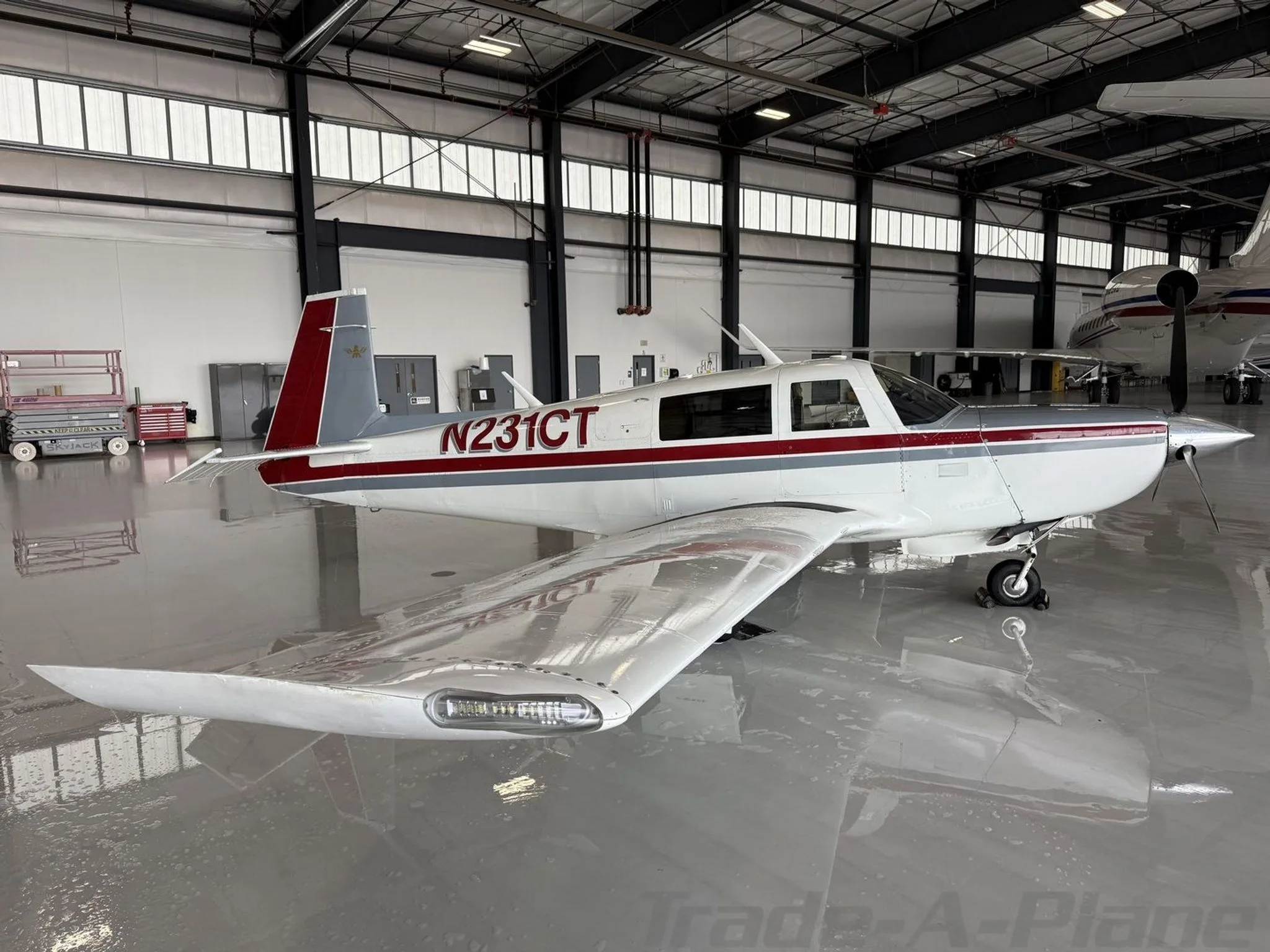 A white, red, and grey single-engine aircraft (N231CT) parked in a hangar.