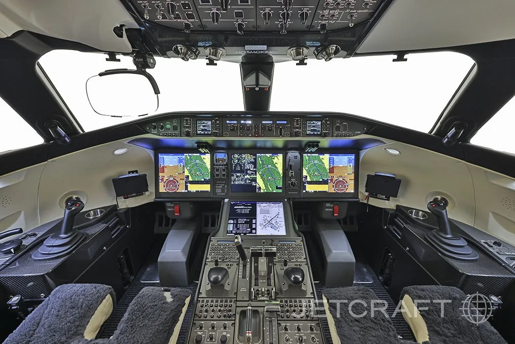 The cockpit of a modern business jet with multiple digital displays and side-stick controls.