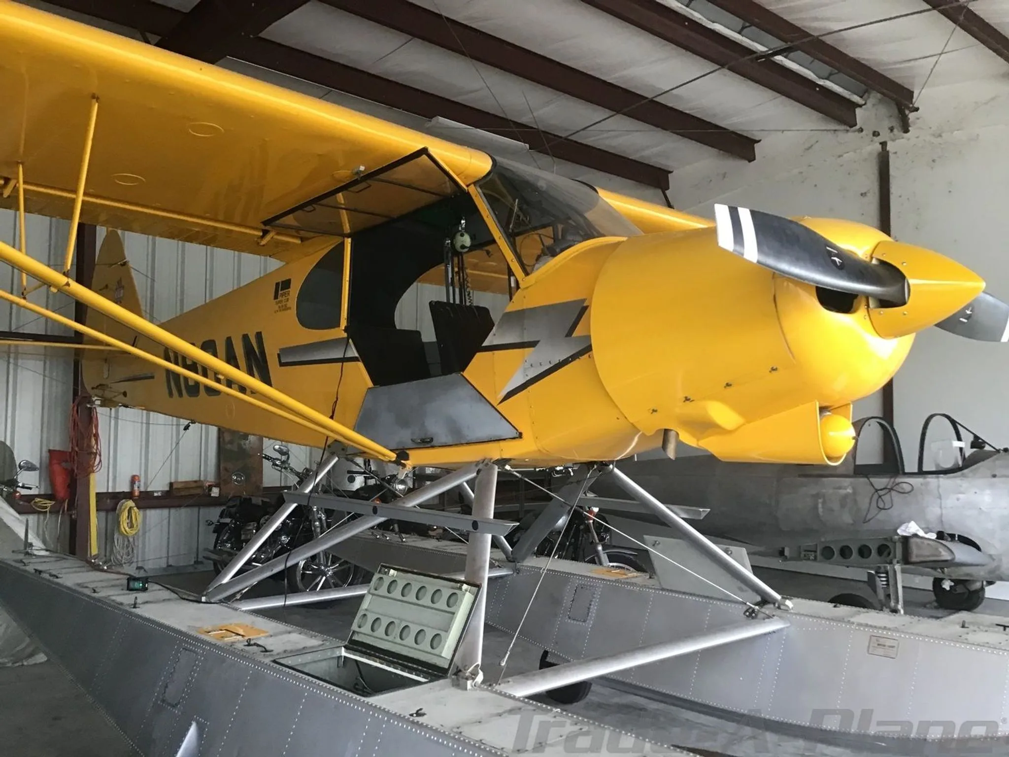 Side view of a yellow Piper Super Cub floatplane (N80AN) with an open door, parked in a hangar.