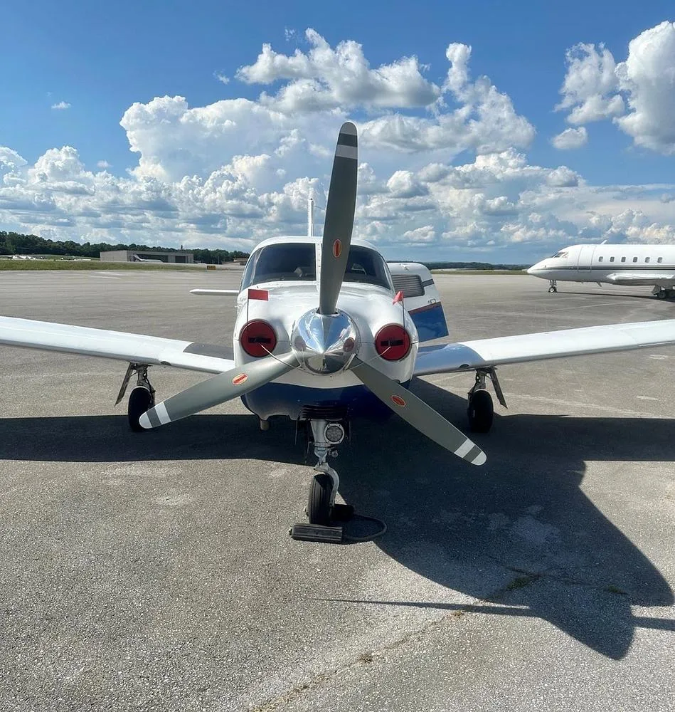 A head-on view of the white and blue Piper Saratoga II TC aircraft, N401BP, with its propeller centered, parked on an airfield.