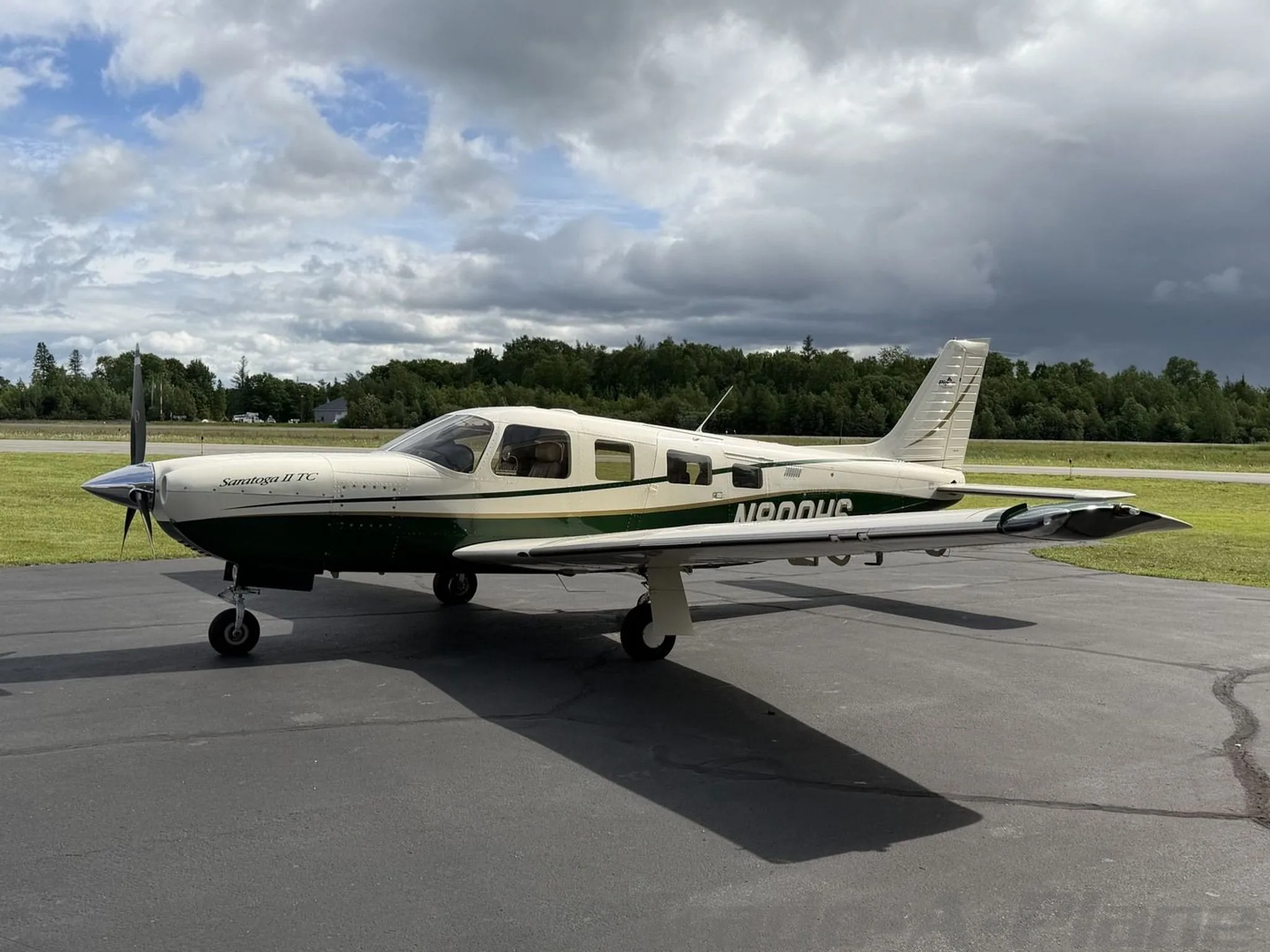 A white and green Piper Saratoga II TC aircraft, registration N800HS, parked on an asphalt ramp with trees in the background under a cloudy sky.