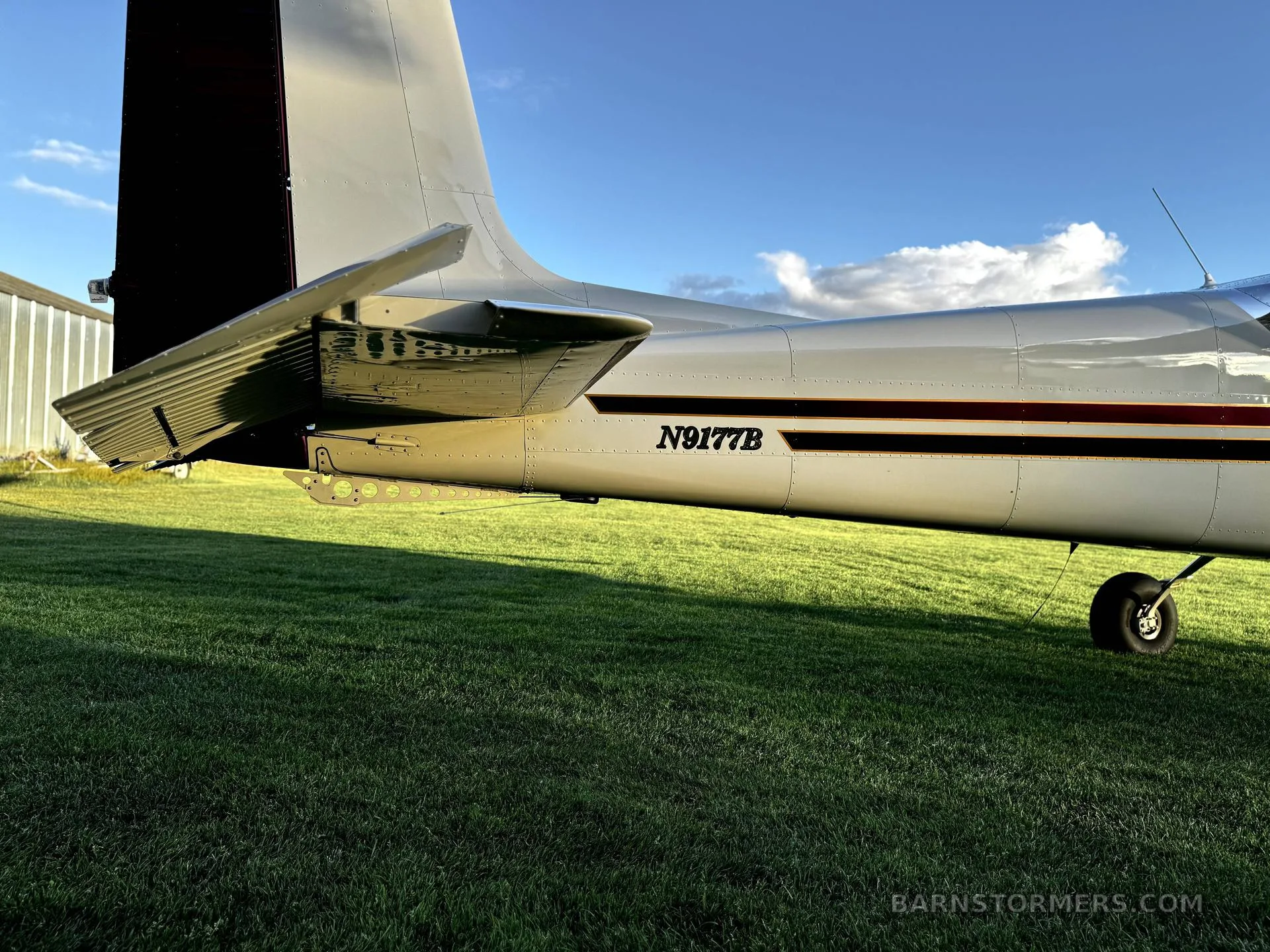 A close-up view of the tail section of a white aircraft with red and black stripes, showing the registration N9177B.