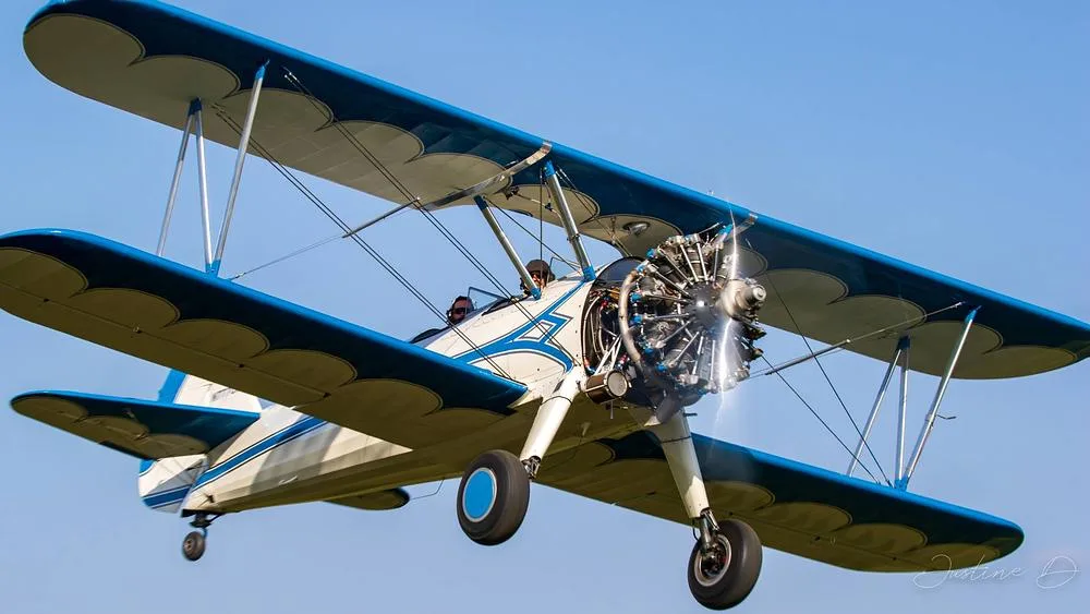 A white and blue biplane with a radial engine in flight against a clear blue sky.
