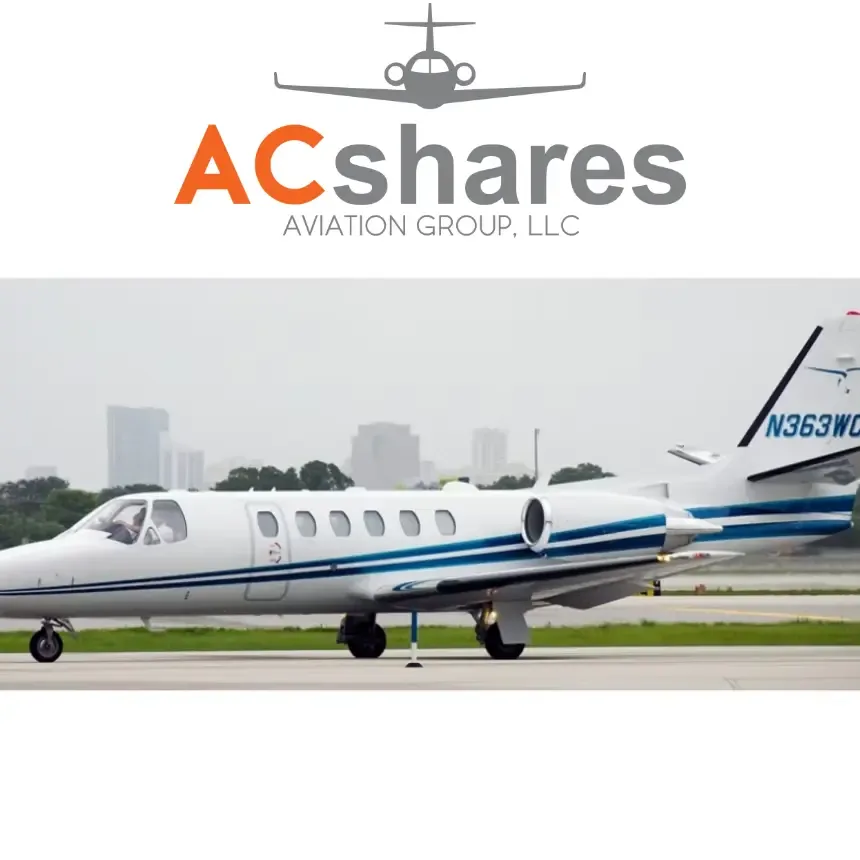 A white business jet with blue stripes and registration N363WC on a tarmac with city buildings in the background.
