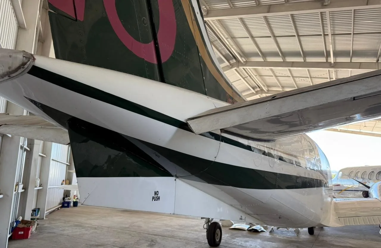 Close-up of the tail and rear fuselage of a white and green King Air C90 aircraft.