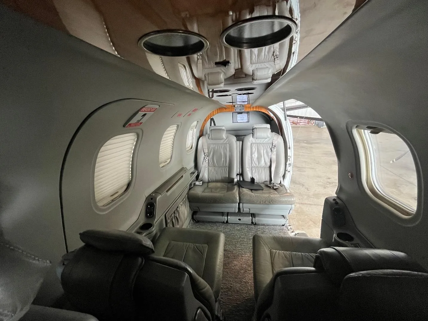 The aircraft cabin interior with light gray leather seats and window shades.