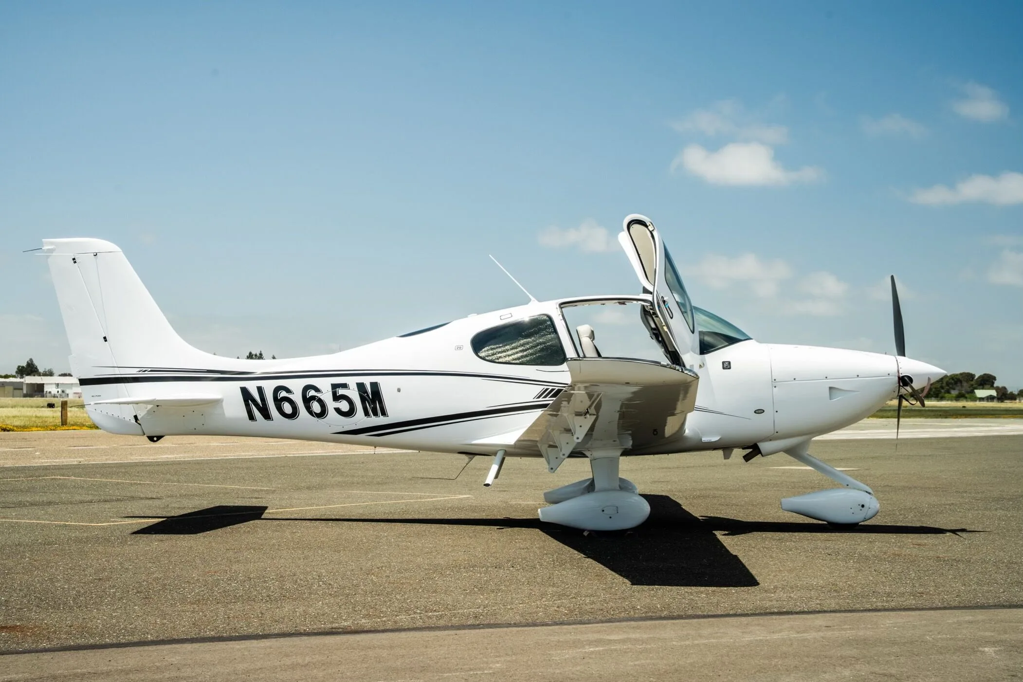 A white Cirrus SR22 aircraft with registration N665M parked on the tarmac with its doors open.