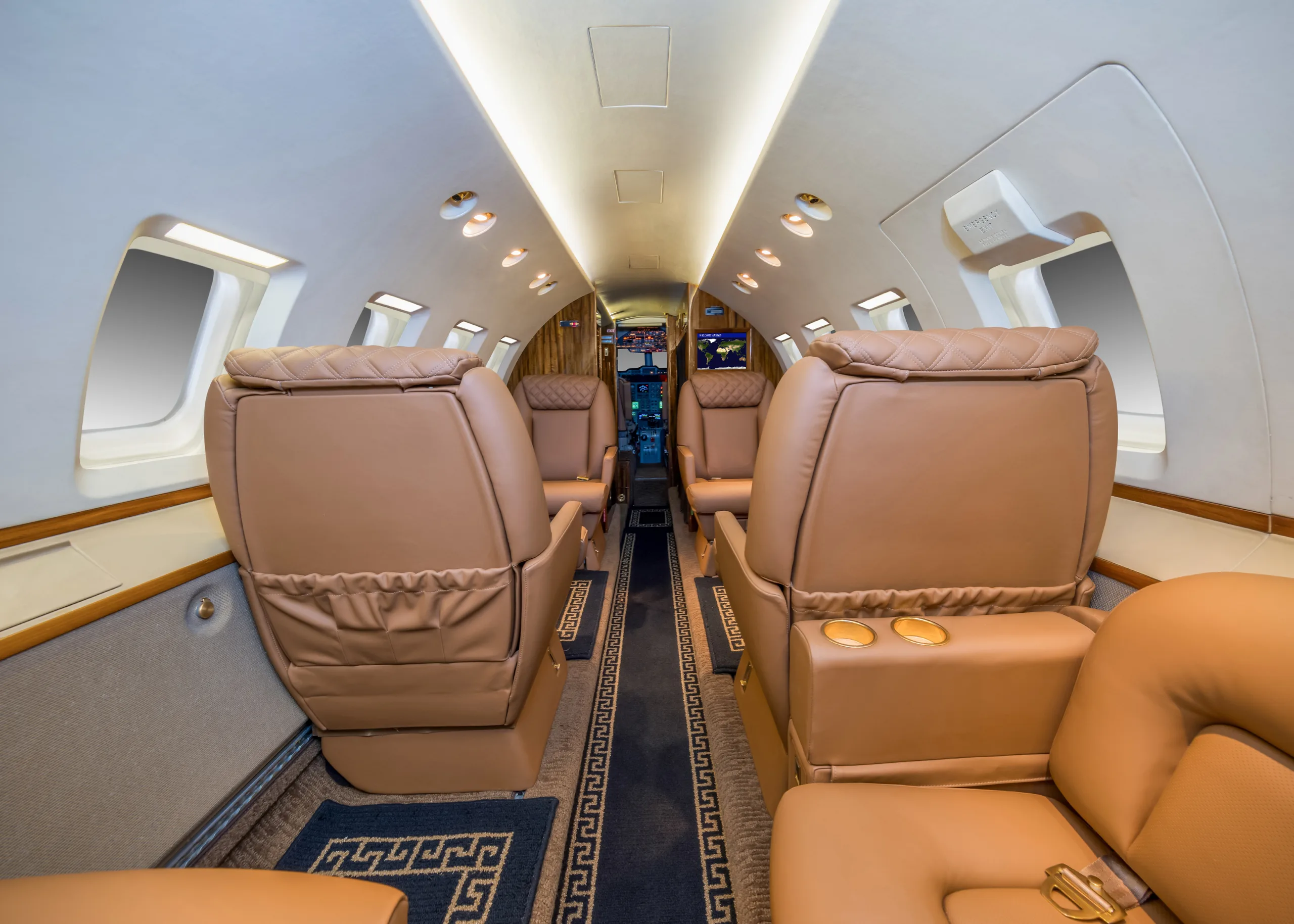 The interior of a private jet cabin, showing tan leather seats and a view towards the rear of the aircraft.