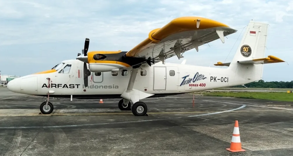 A side view of a white and yellow Airfast Indonesia Twin Otter Series 400 aircraft (PK-OCI) with its wing flaps extended, parked on an airfield.