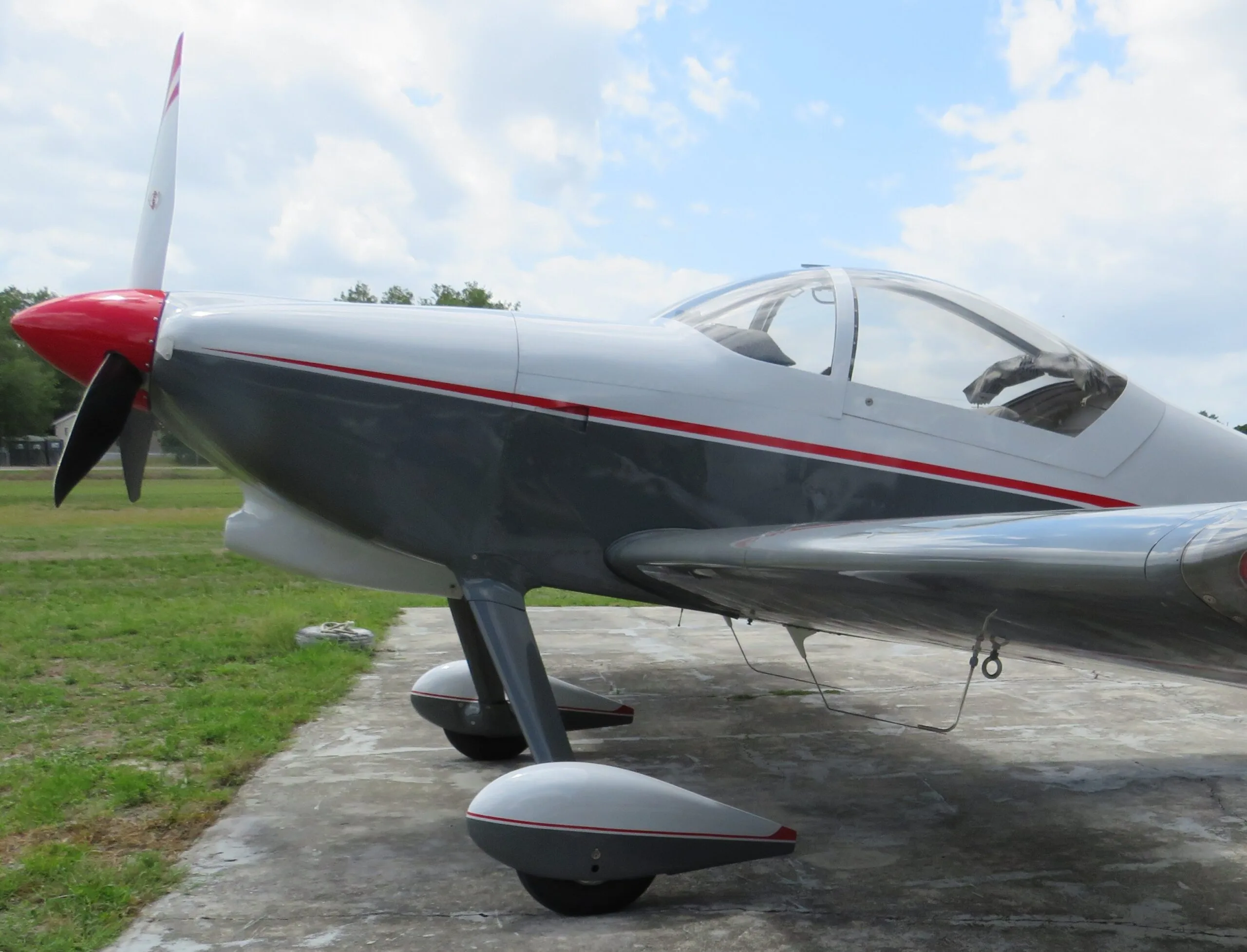 Side view of a white and grey aircraft with red accents on the propeller and stripes, parked on concrete.