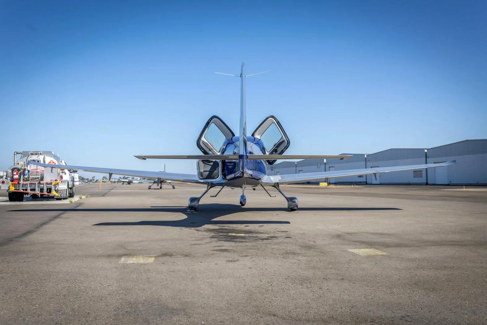 A rear view of the blue and silver Cirrus SR22 aircraft, N275MG, with its doors open on the tarmac.