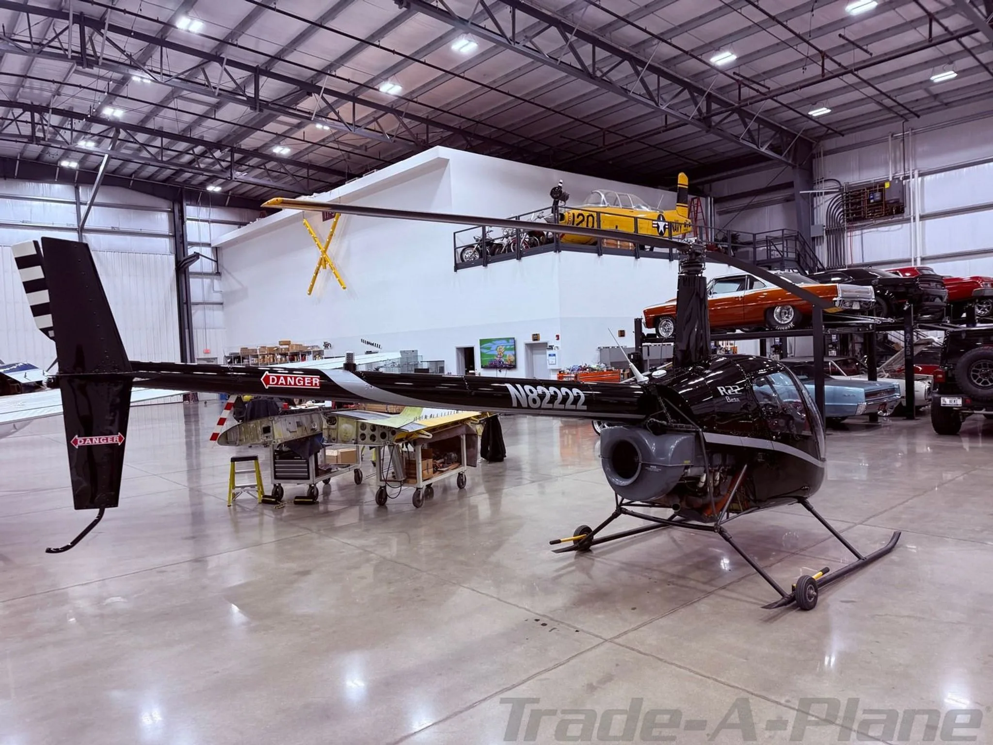 A side view of the black Robinson R22 Beta helicopter, N82222, with a white stripe on the tail, in a hangar.
