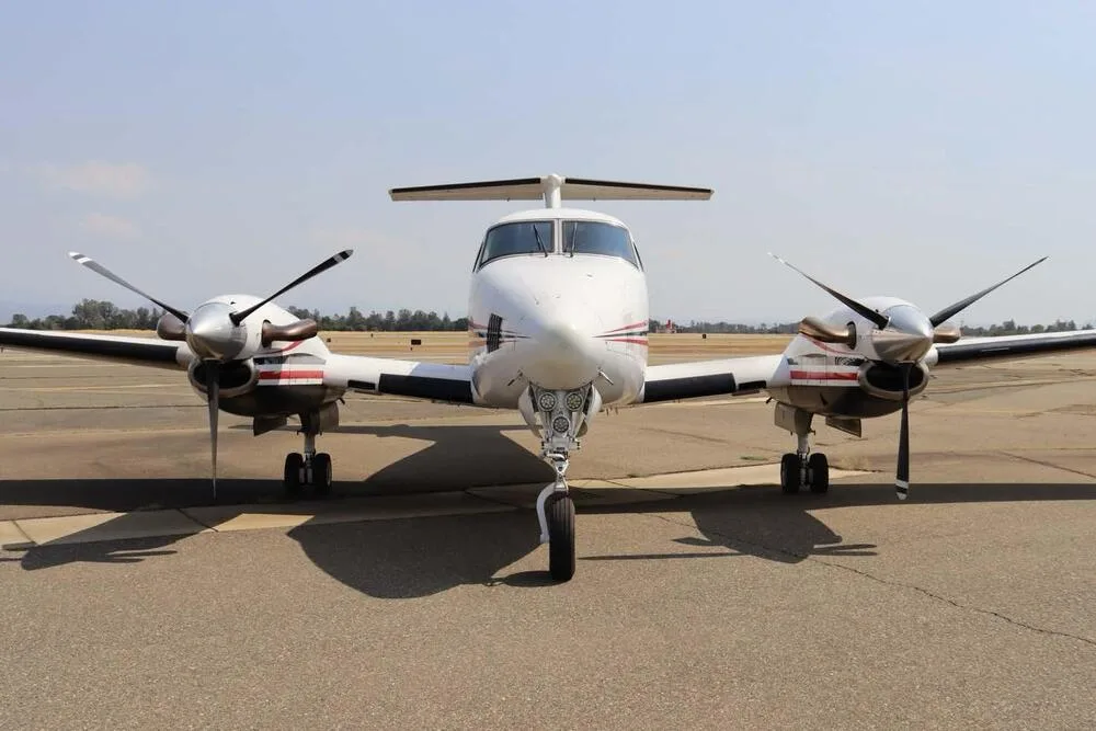 Head-on view of a white Beechcraft King Air with red and black stripes on an airport tarmac.