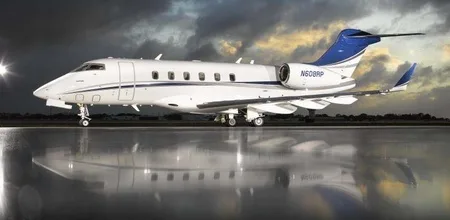 A white business jet with blue tail accents sits on a wet tarmac under a dramatic cloudy sky.