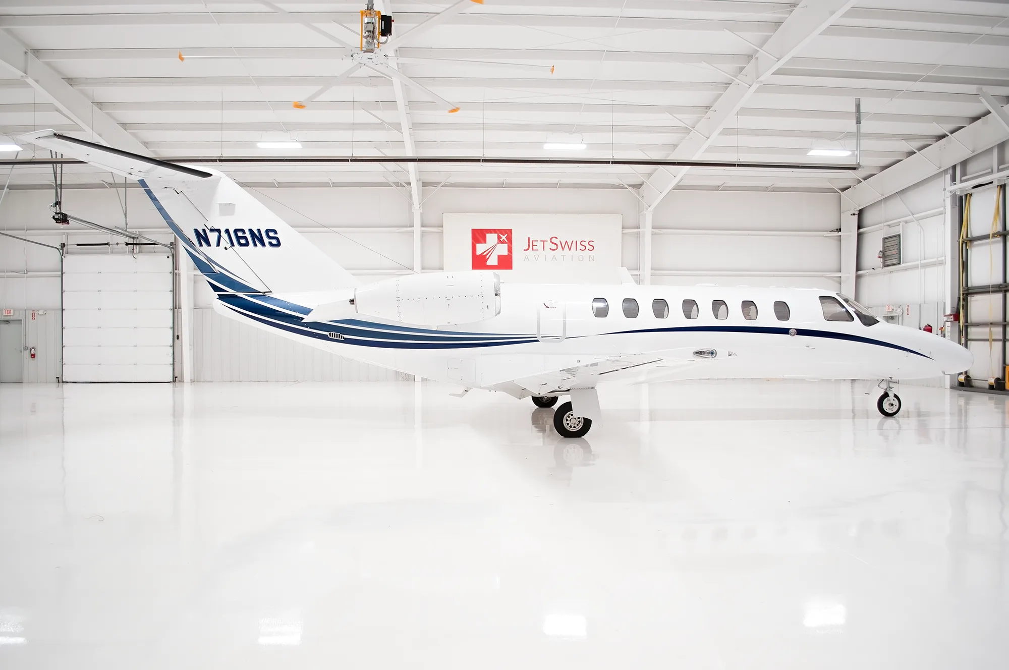 A side view of a white Cessna Citation business jet with blue stripes, registration N716NS, in a hangar.